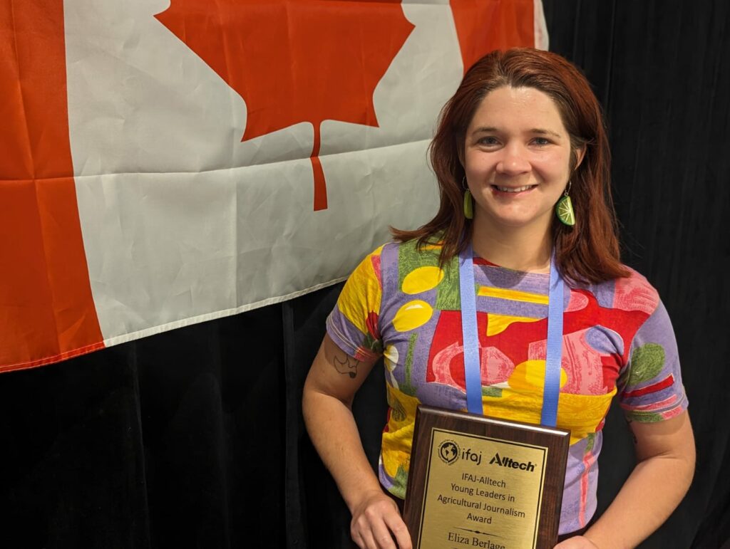 Eliza Berlage stands in front of a Canadian flag holding her award plaque
